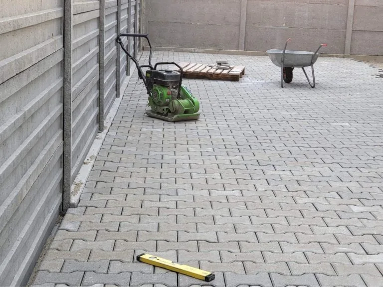 Szürke behaton térkő udvar lapvibrátorral és vízmértékkel tömörítés előtt