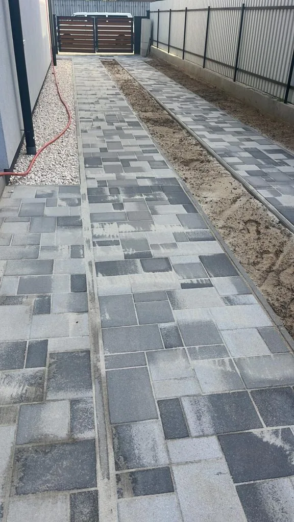 Melírozott szürke kombi térkő járda családi ház és kerítés között, kavicssávval