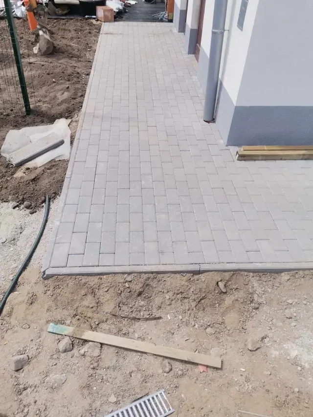 Szürke téglakő járda futókötésben, beton szegéllyel egy új családi ház mellett