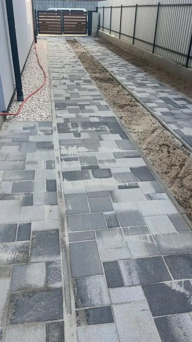 Melírozott szürke kombi térkő járda családi ház és kerítés között, kavicssávval