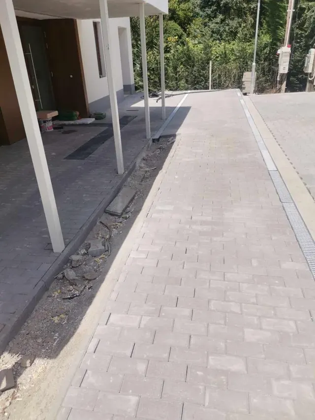 Téglakő bejárati út vonalas folyókával a fedett beálló és a ház között